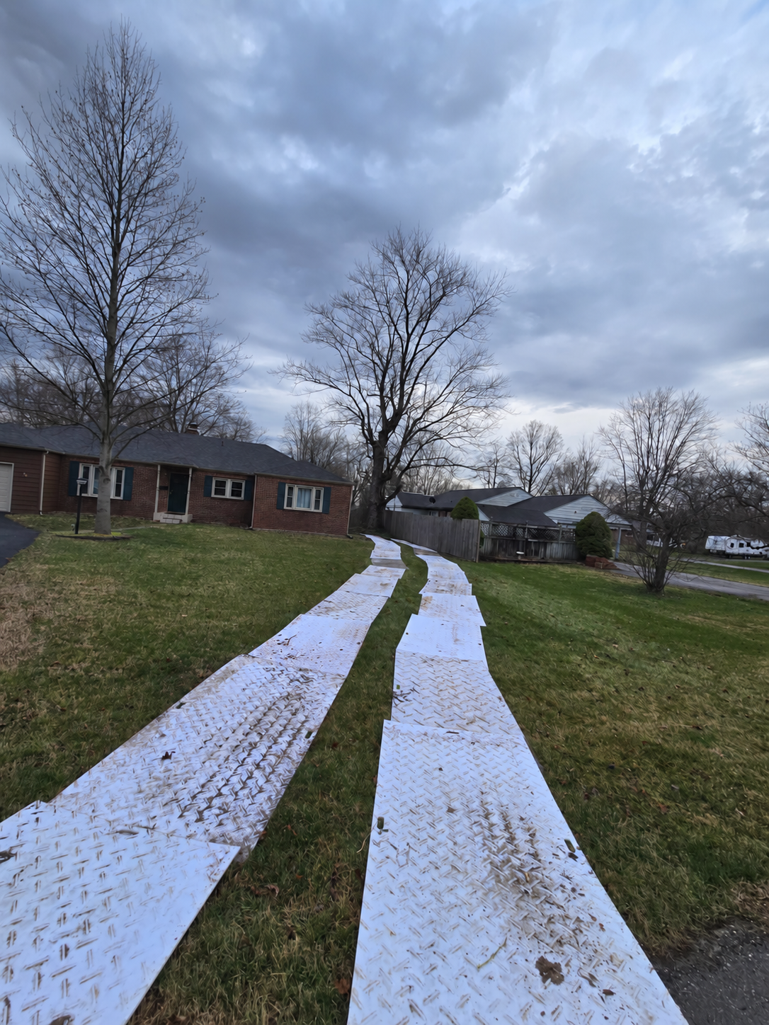 Two lanes of white ground protection mats creating an equipment route across a residential lawn